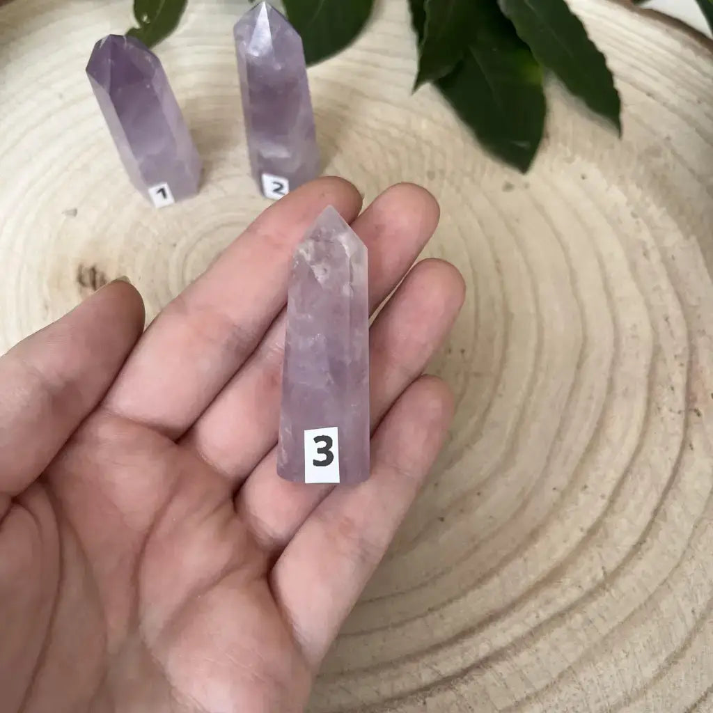 Pointe d'Améthyste en Pointe tenue dans une main, avec d'autres pierres en arrière-plan