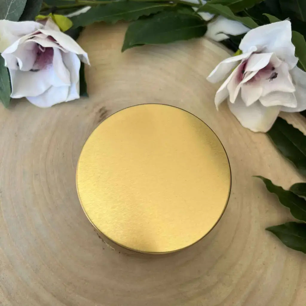 Bougie Amour en quartz rose Aura de Roche dans boîte dorée sur tranche de bois entourée de fleurs blanches