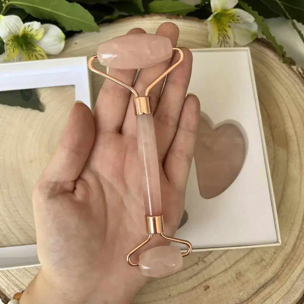 Coffret Gua sha et Rouleau de massage en Quartz rose avec poignée en métal rose, sur un fond naturel.