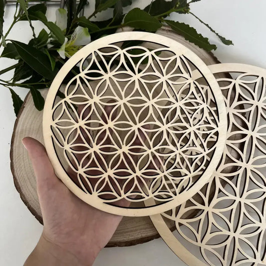 Plaque Fleur de Vie en Bois tenue à la main sur un fond naturel avec des éléments de décoration.