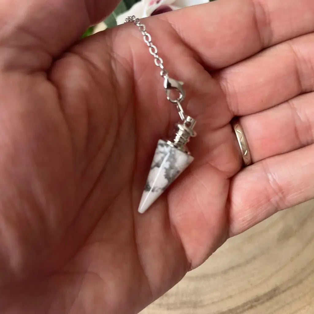 Pendule en Howlite Blanche conique monté sur chaîne argentée tenu dans la main Aura de Roche