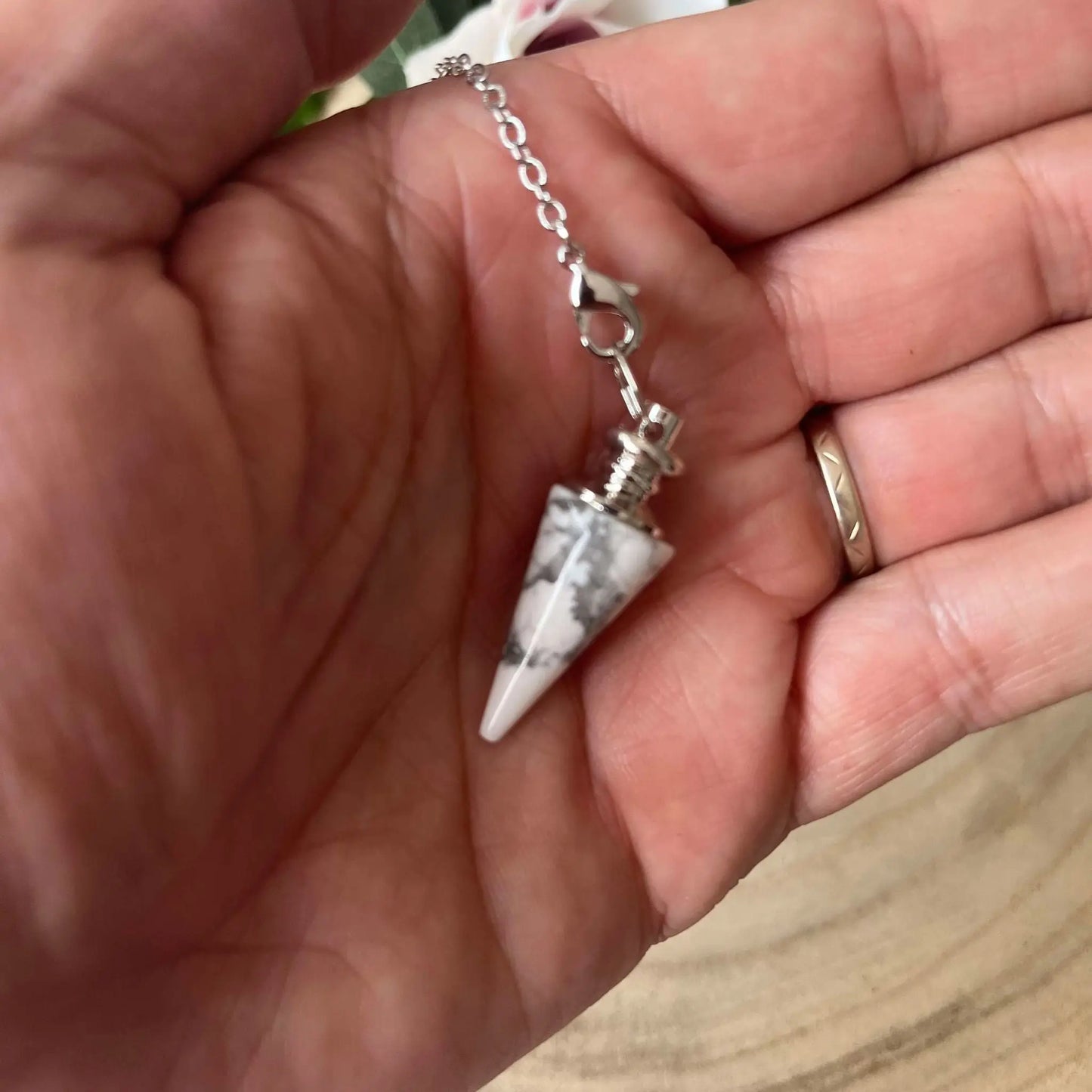 Pendule en Howlite Blanche conique monté sur chaîne argentée tenu dans la main Aura de Roche