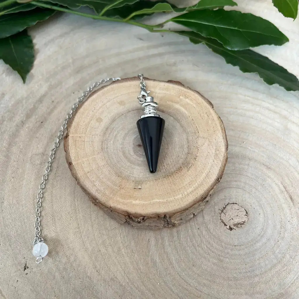 Pendule en Obsidienne Noire conique avec monture argentée et chaîne posé sur rondin de bois
