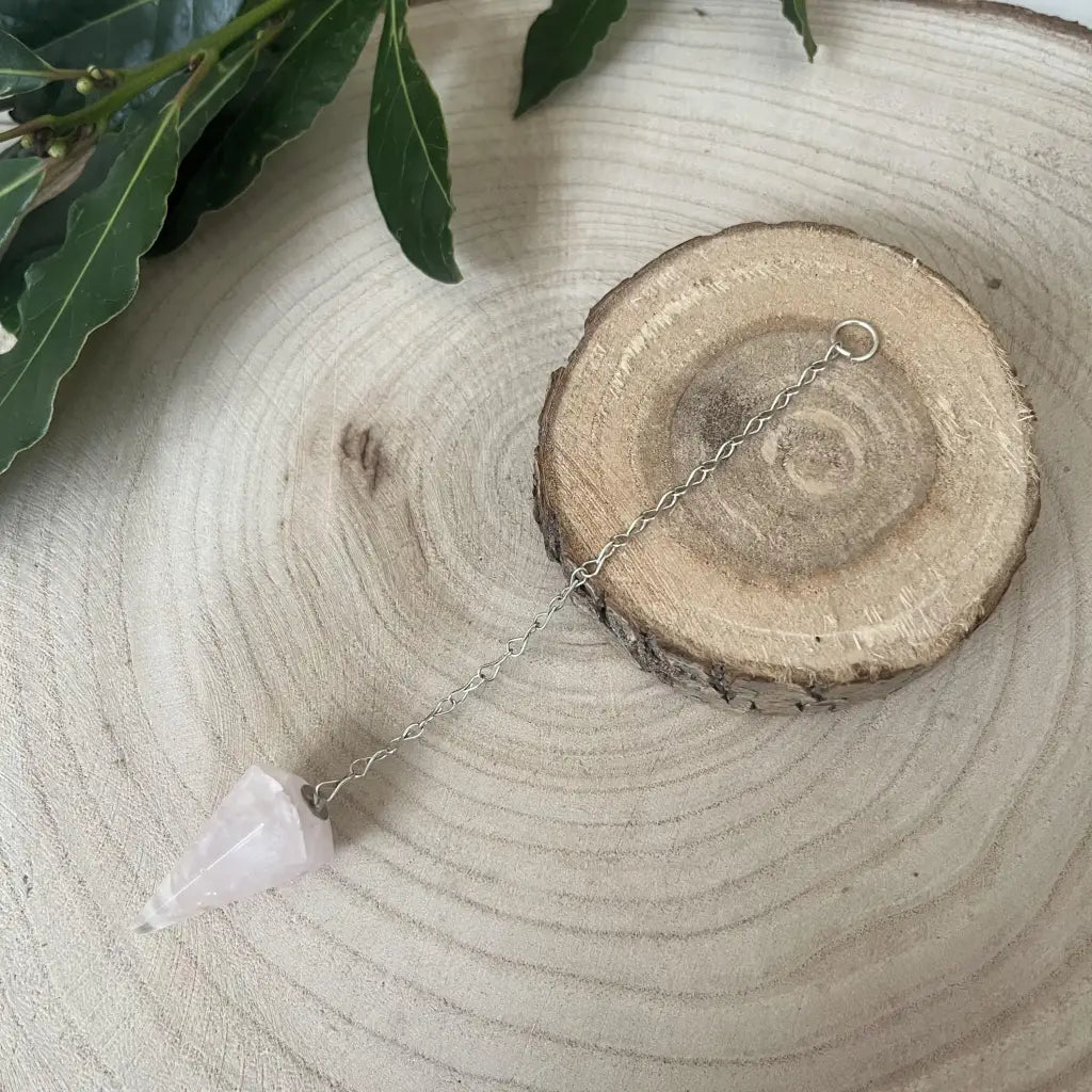 Pendule en Quartz Rose Aura de Roche pointu sur chaine metal posé sur tranche de bois avec feuillage