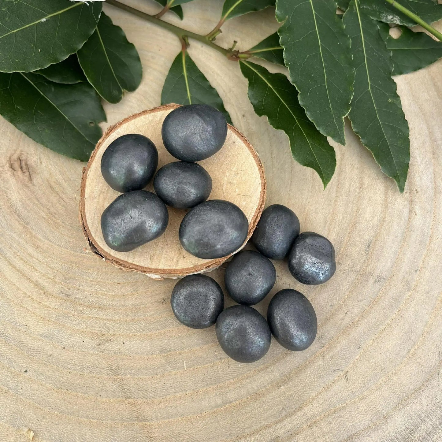 Shungite pierre roulée naturelle lisse gris foncé dans un bol en bois rustique pour purification et protection