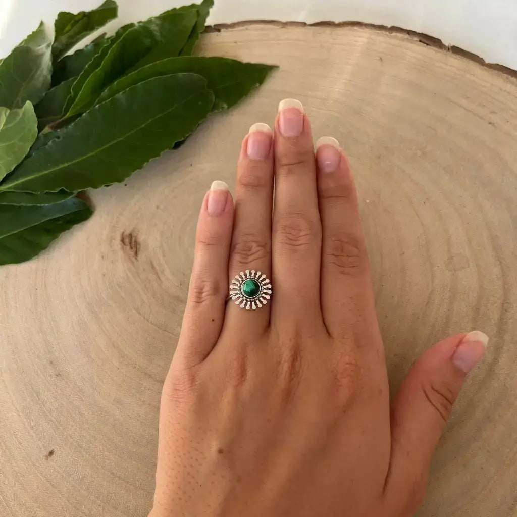 Bague ajustable Fleur en argent avec pierre verte portée sur la main sur fond bois et feuilles