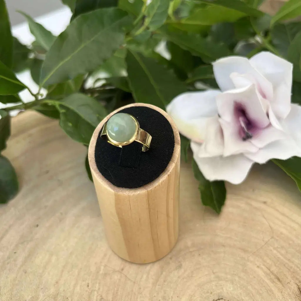 Bague ajustable ronde Dorée avec pierre verte sur présentoir en bois et fleurs blanches