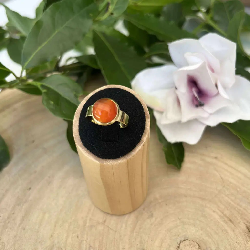 Bague ajustable ronde Dorée avec pierre orange présentée sur socle en bois Aura de Roche