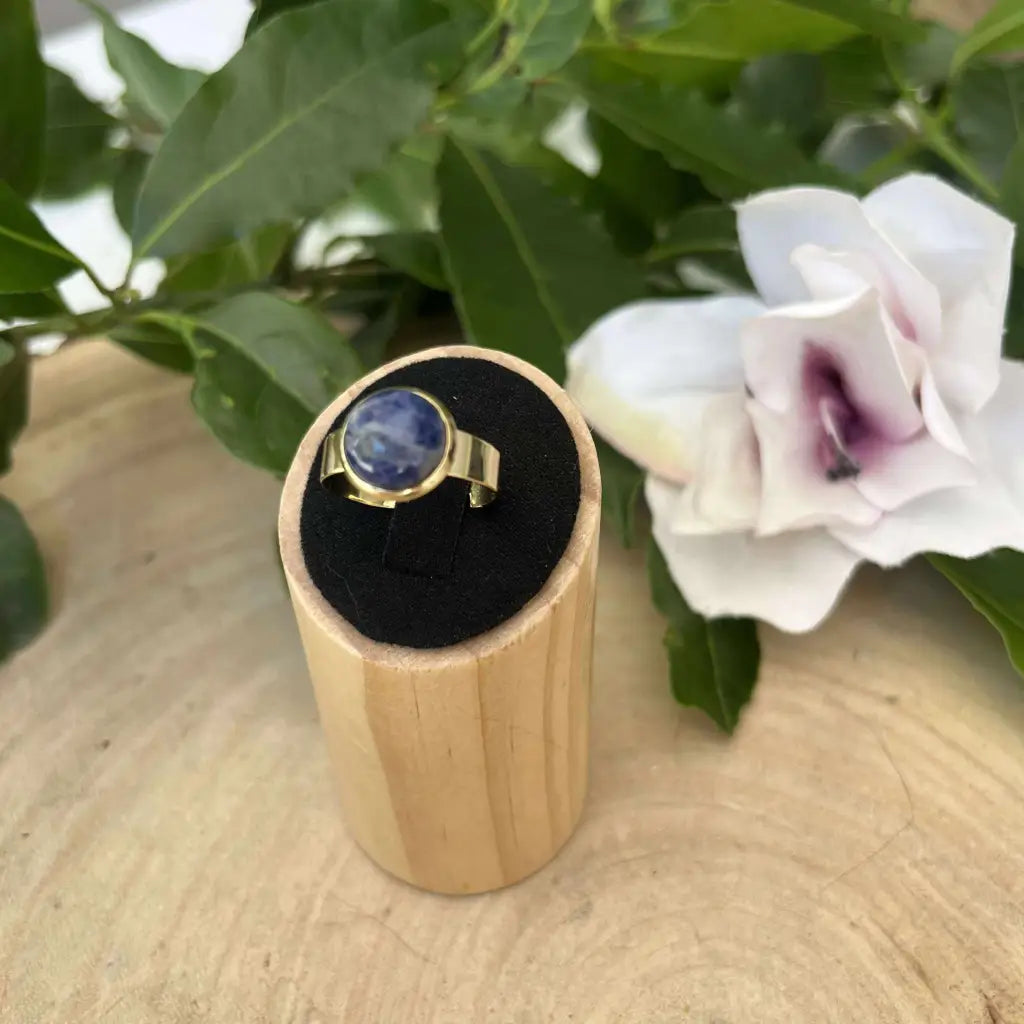 Bague ajustable ronde Dorée avec pierre bleue posée sur présentoir en bois Aura de Roche