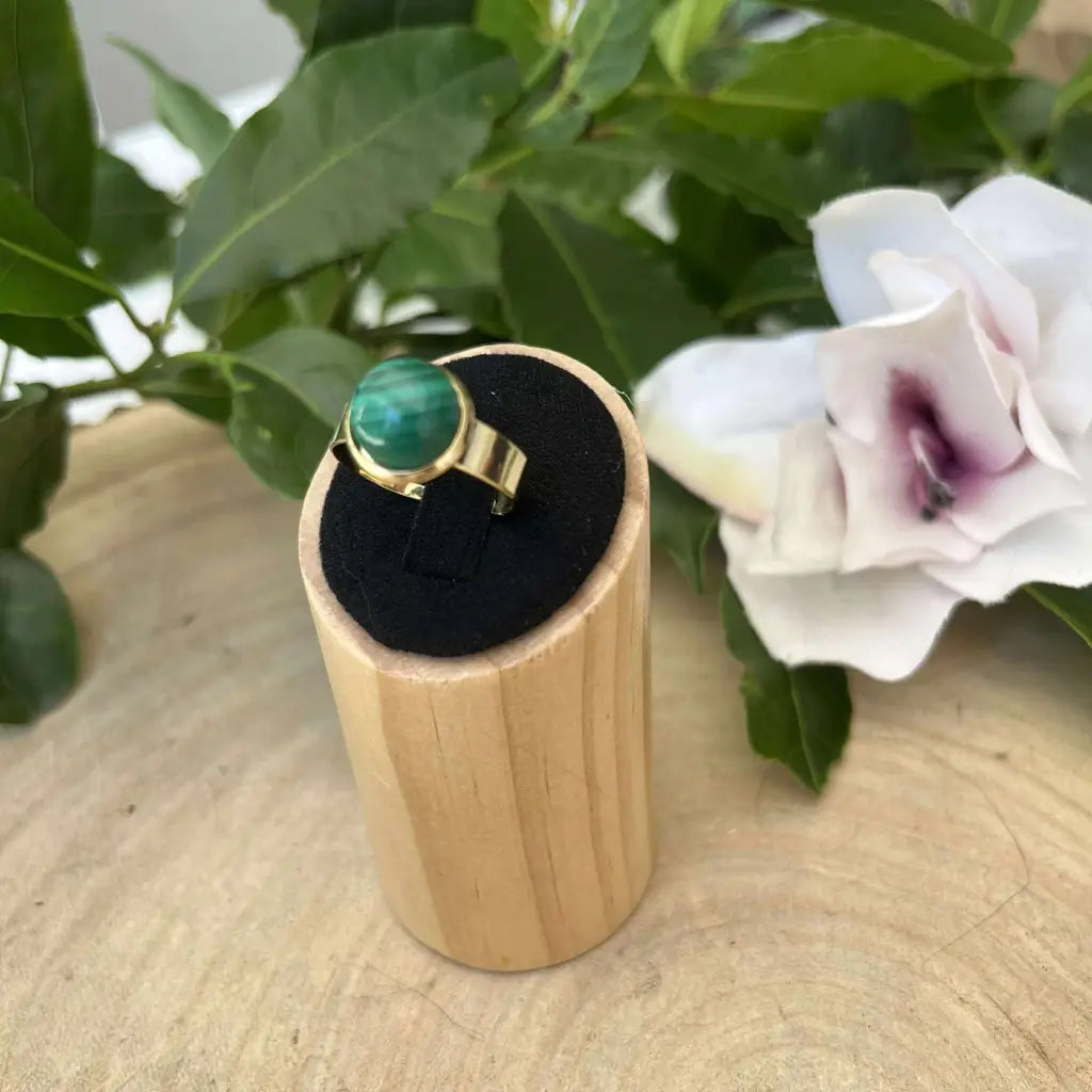 Bague ajustable ronde Dorée avec pierre verte sur support en bois et décor floral