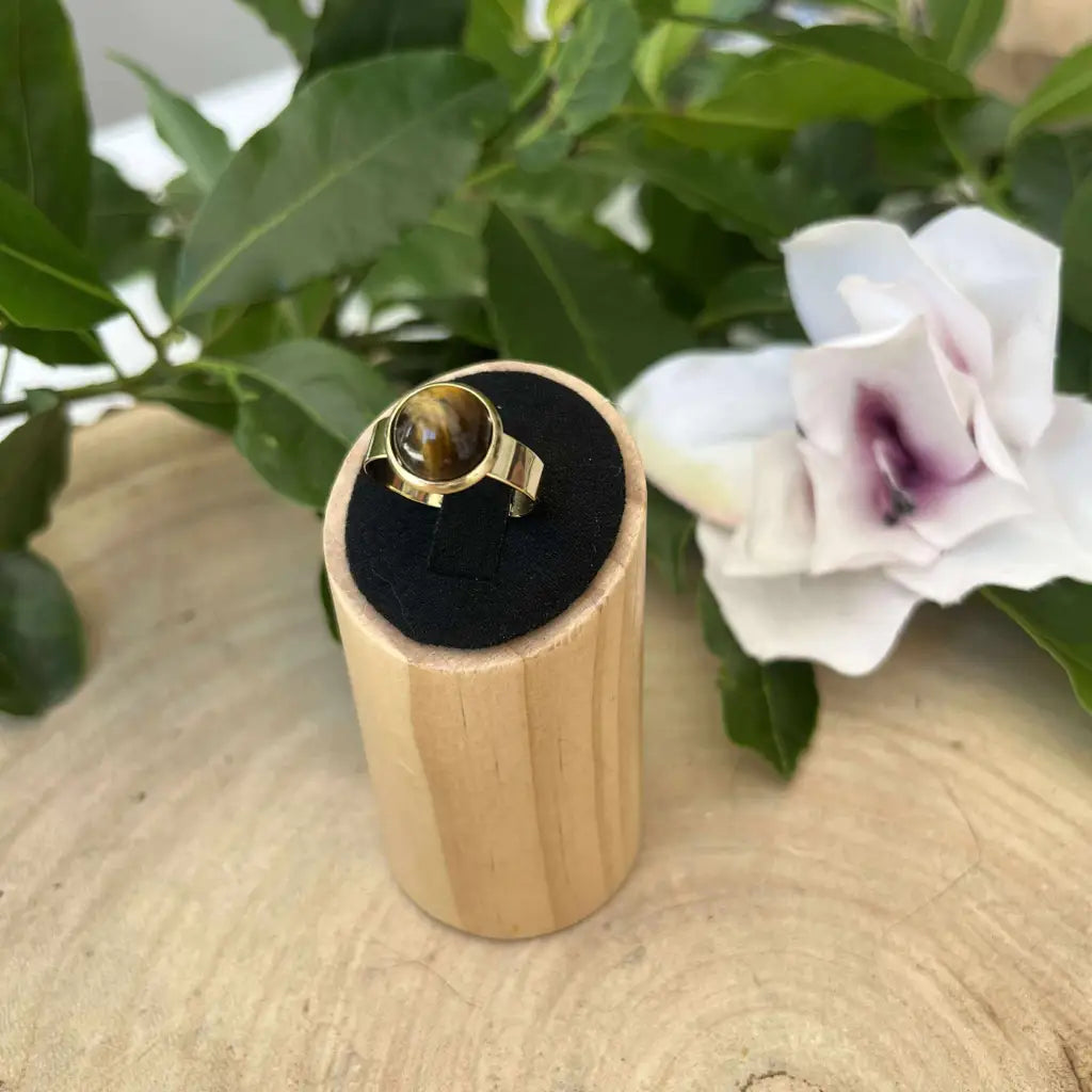 Bague ajustable ronde Dorée avec pierre centrale posée sur support en bois noir Aura de Roche