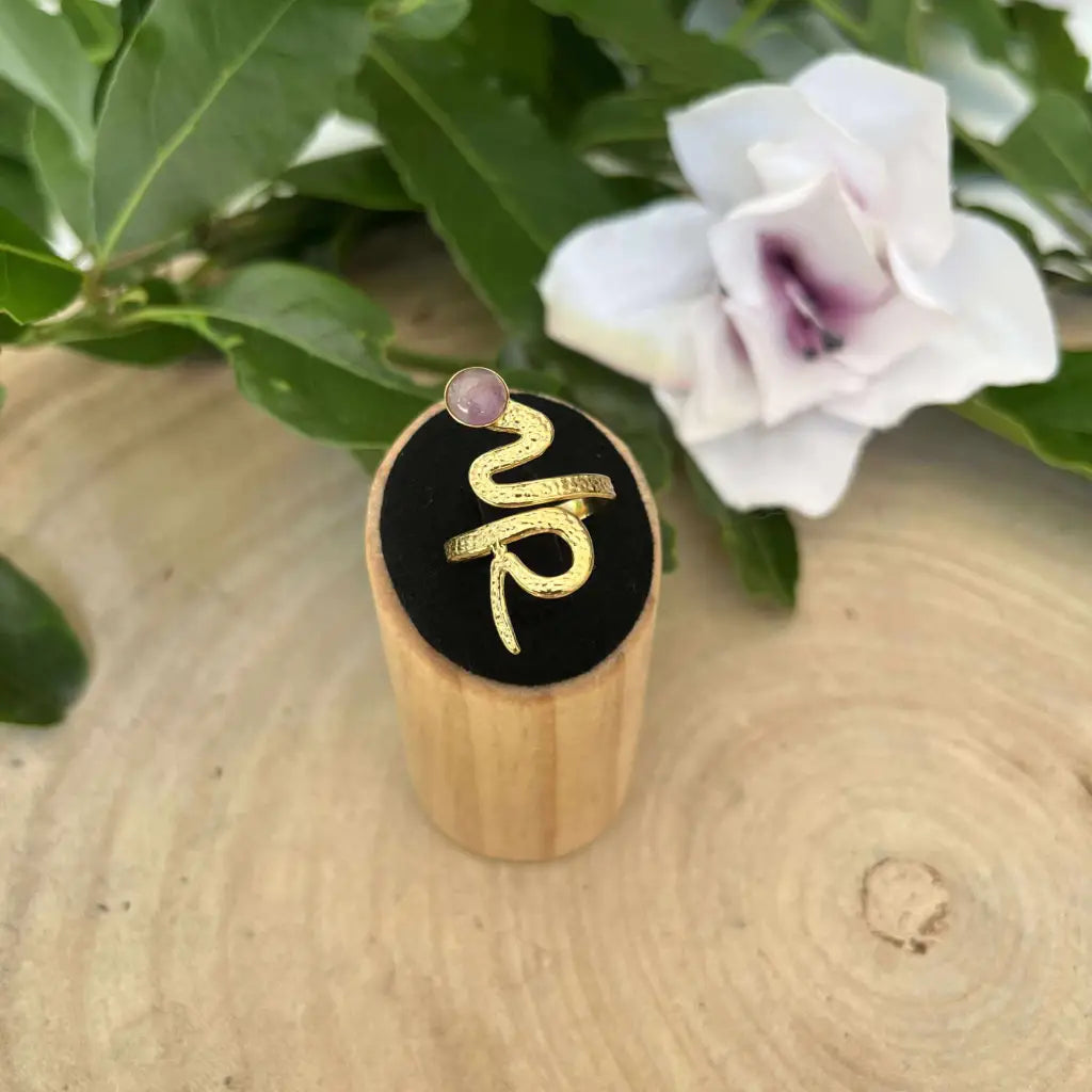 Bague ajustable Serpent dorée avec pierre rose sur support en bois par Aura de Roche