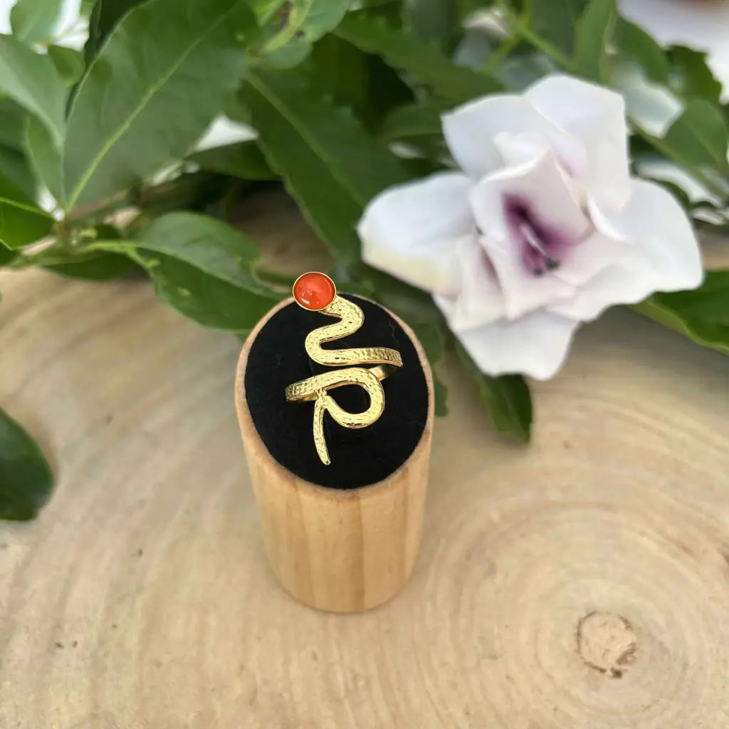 Bague ajustable Serpent en métal doré avec pierre rouge sur support en bois par Aura de Roche