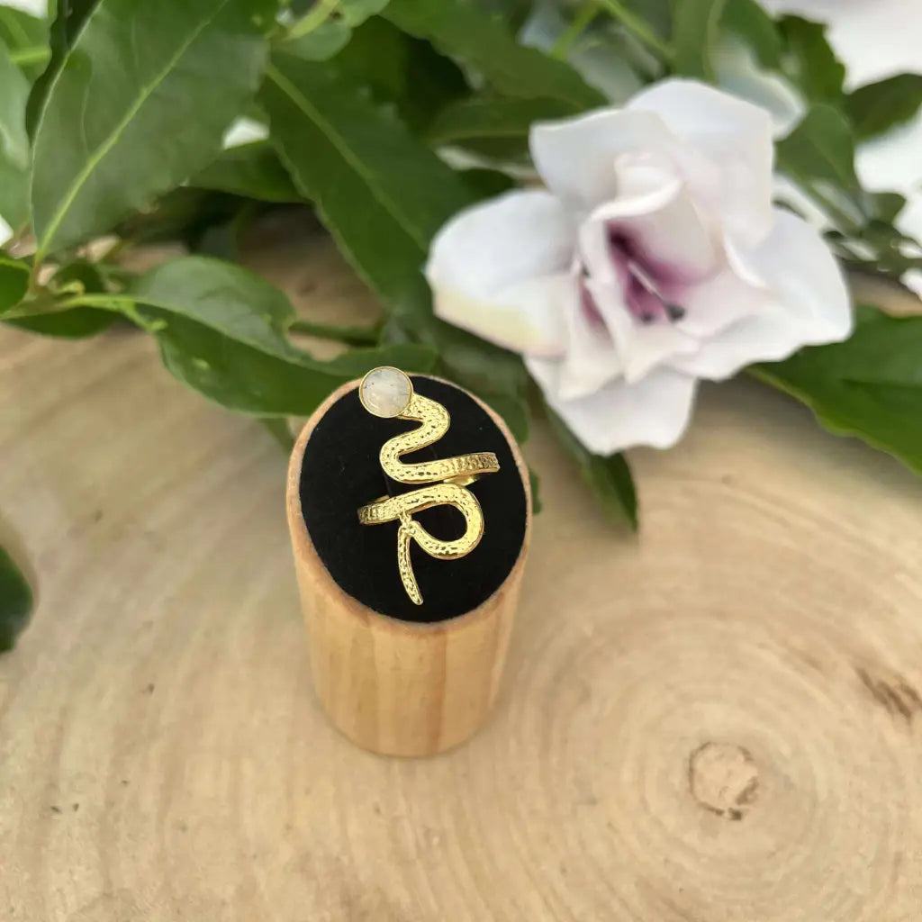 Bague ajustable Serpent dorée avec pierre blanche présentée sur support en bois par Aura de Roche