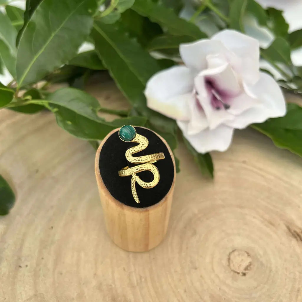 Bague ajustable Serpent dorée avec pierre verte présentée sur support en bois et fond naturel