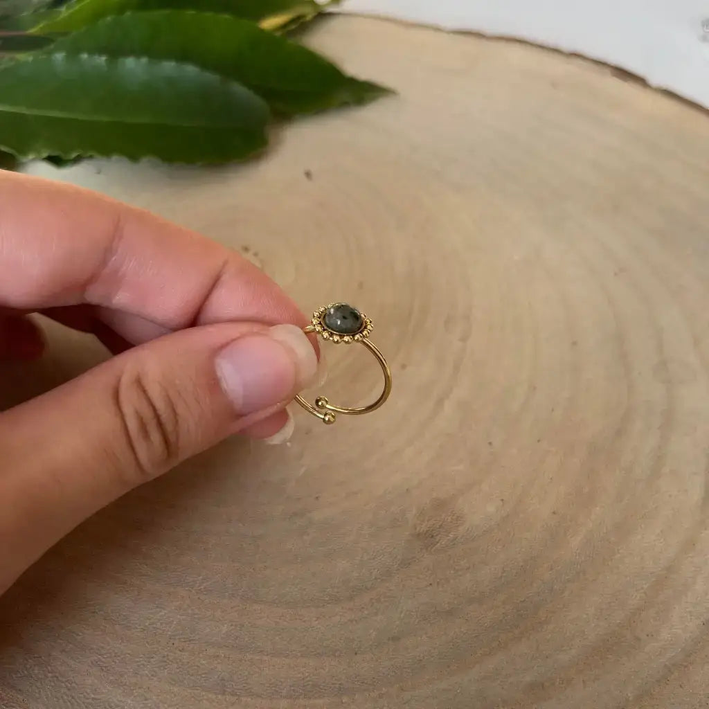 Bague ajustable Solara en métal doré avec pierre verte tenue à la main sur fond naturel