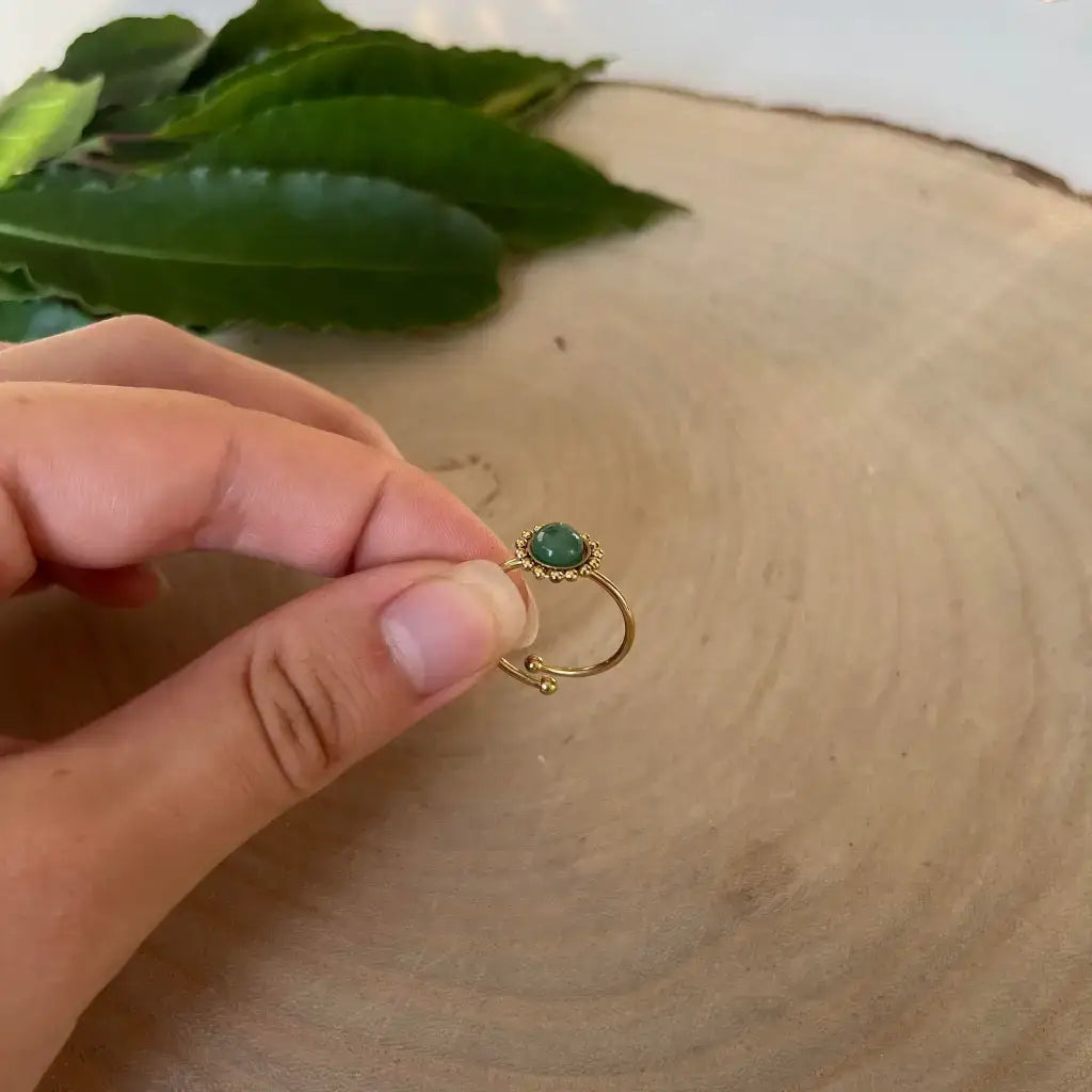 Bague ajustable Solara en or avec pierre verte tenue à la main sur un fond en bois naturel