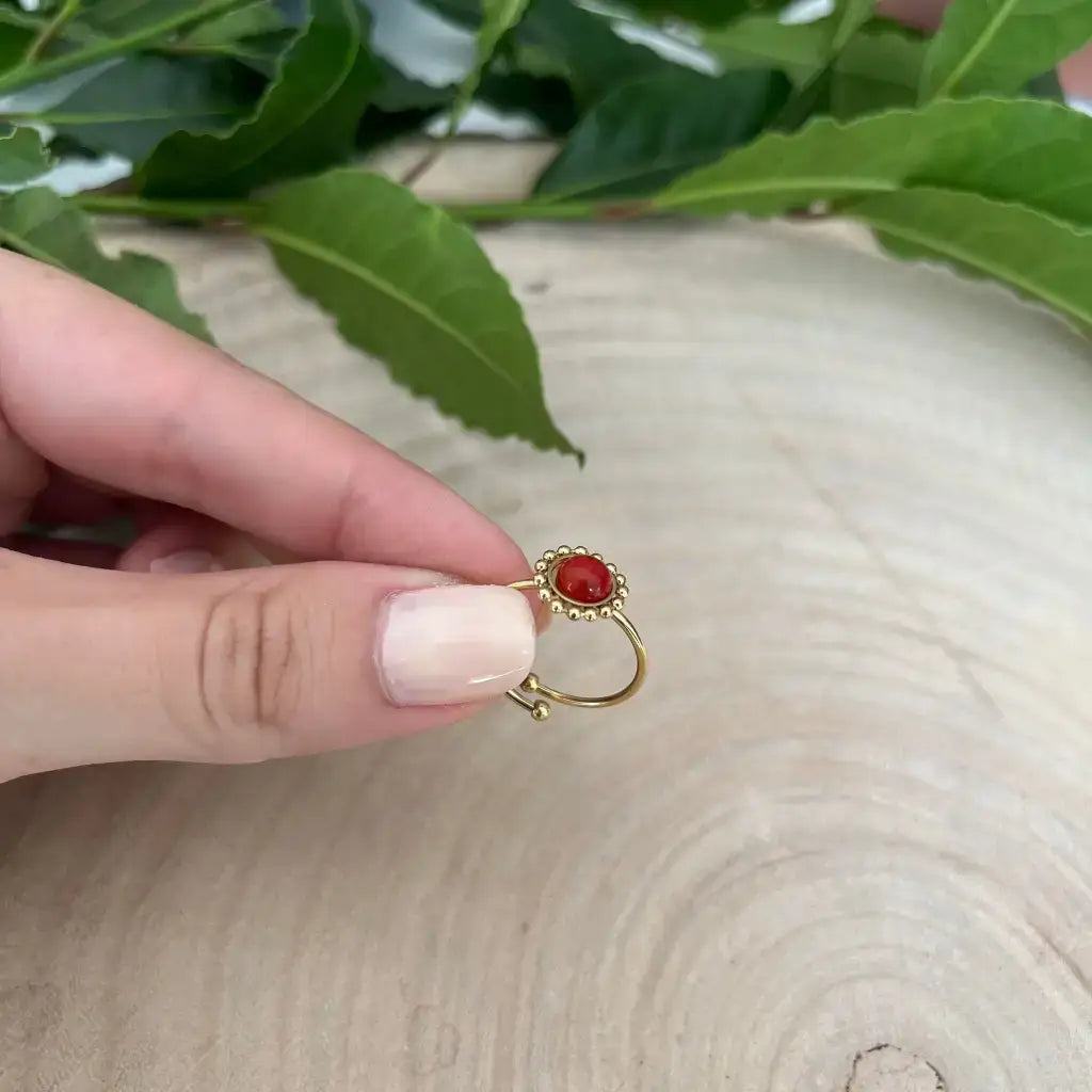 Bague ajustable Solara dorée avec pierre rouge portée par une main sur fond naturel