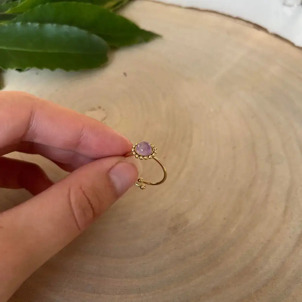 Bague ajustable Solara en or avec pierre violette portée à la main sur fond en bois naturel