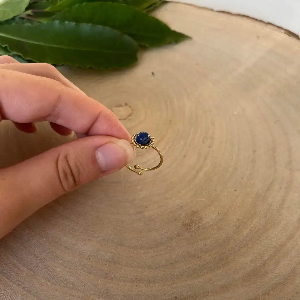 Bague ajustable Solara en or avec pierre bleue portée sur un doigt sur fond en bois