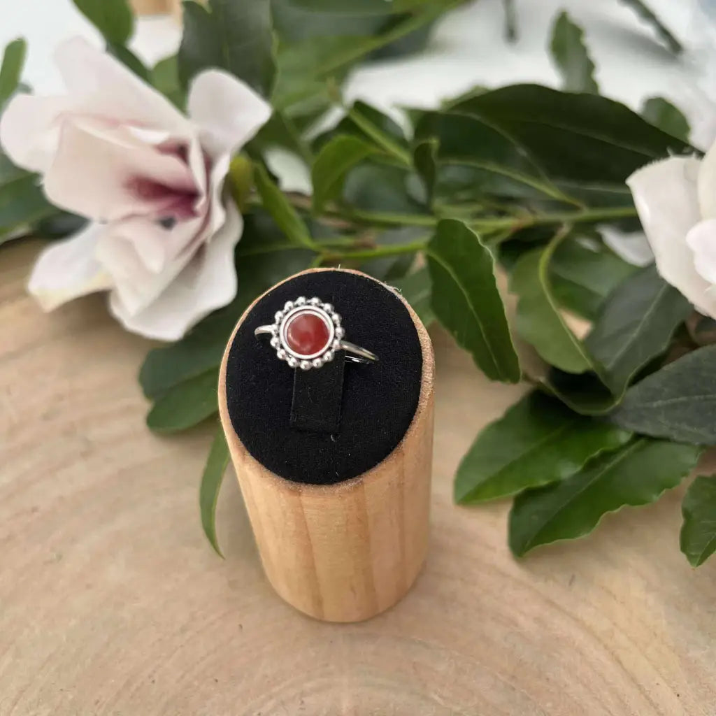 Bague ajustable Solara d'Aura de Roche en argent avec pierre rouge sur présentoir en bois et fleurs