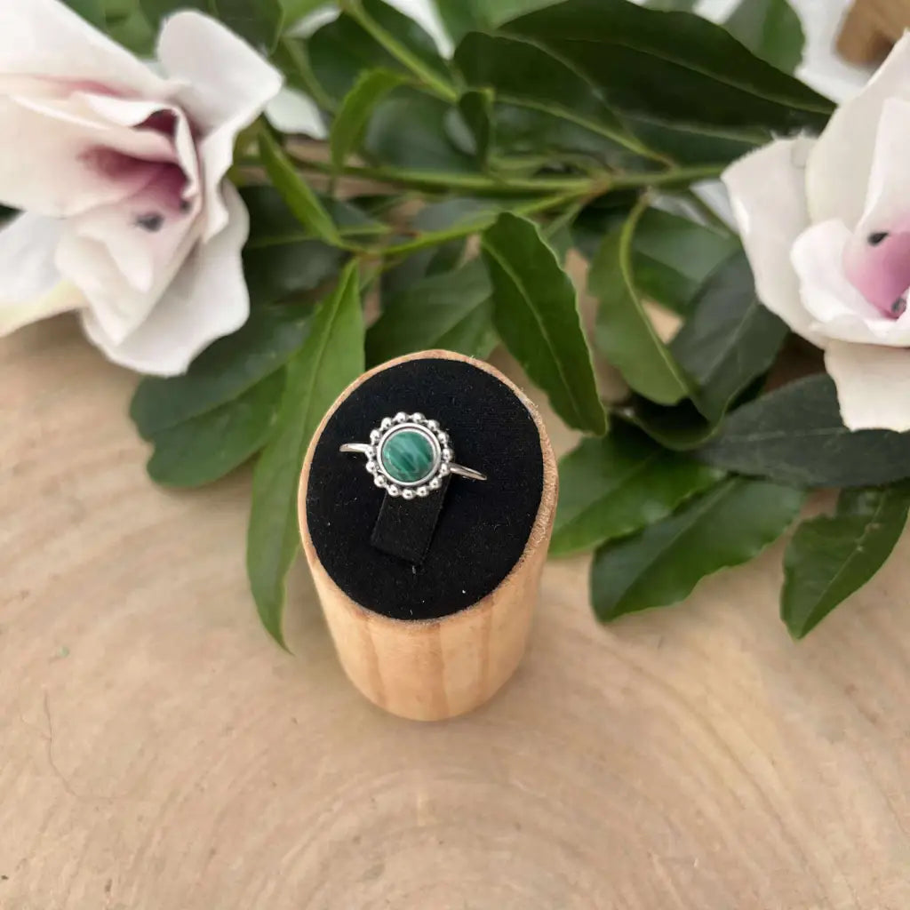 Bague ajustable Solara avec pierre verte sertie sur métal argenté présentée sur support en bois