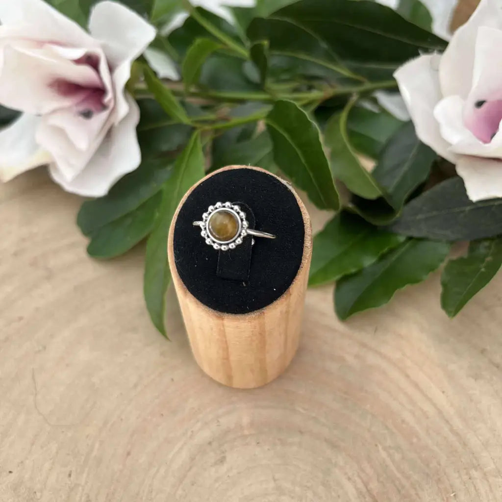 Bague ajustable Solara en argent avec pierre ronde verte sur présentoir en bois et fleurs blanches