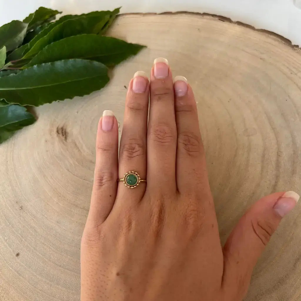 Bague ajustable Solara avec pierre verte portée sur la main sur fond en bois et feuilles vertes