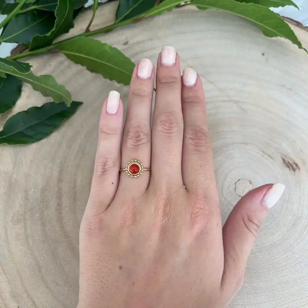 Bague ajustable Solara en or avec pierre rouge portée sur la main féminine posée sur bois naturel