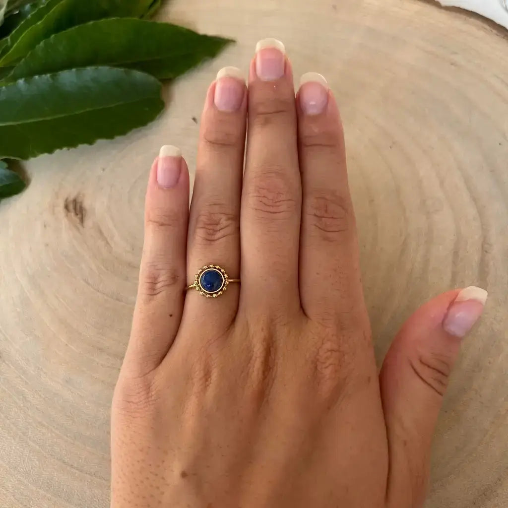 Bague ajustable Solara en or avec pierre bleue portée sur une main posée sur une surface en bois