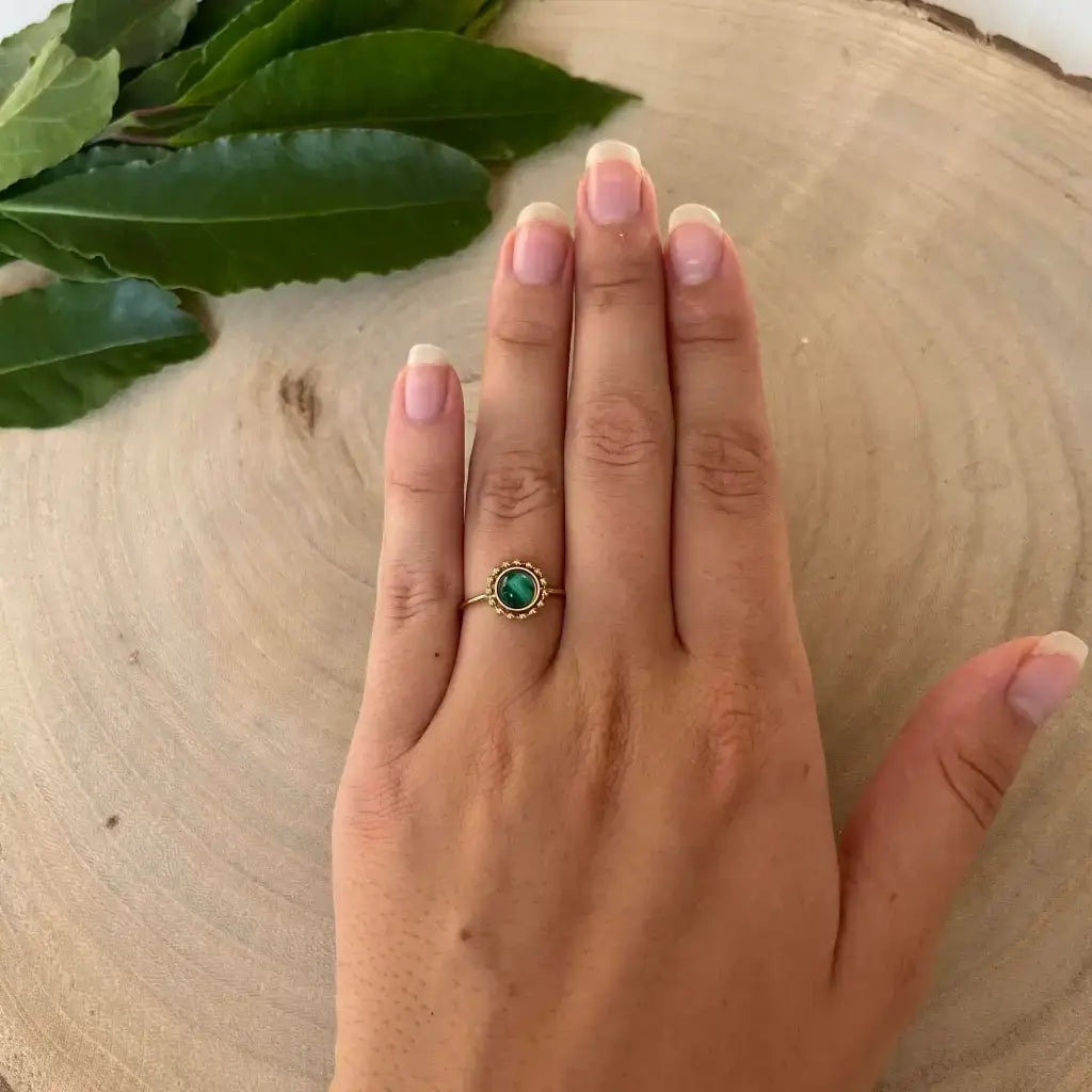 Bague ajustable Solara Aura de Roche avec pierre verte portée sur une main posée sur bois