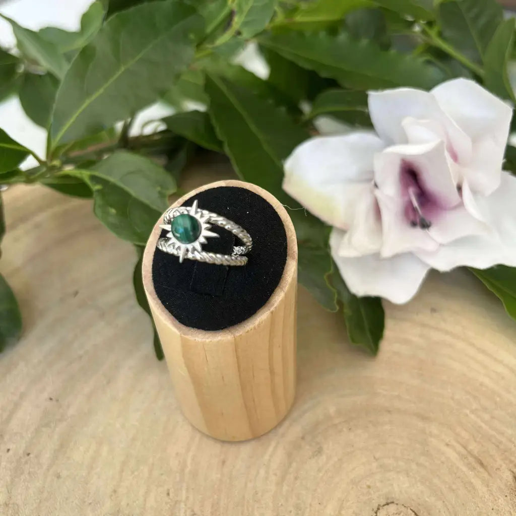 Bague ajustable Soleil en argent avec pierre verte présentée sur support en bois avec fleurs blanches