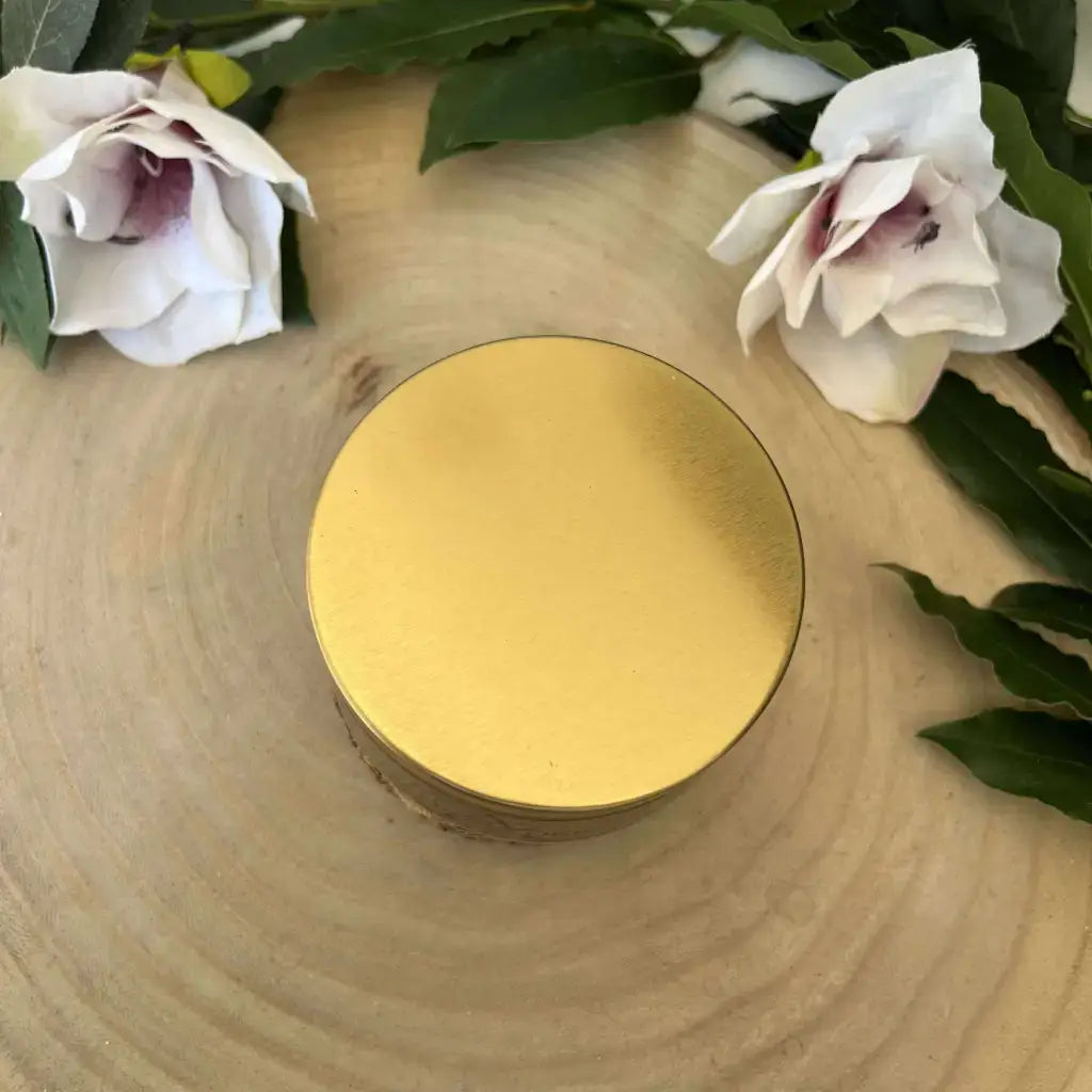 Bougie Mauvais Œil Aura de Roche dans boîte dorée sur tranche de bois avec fleurs blanches et pierre naturelle