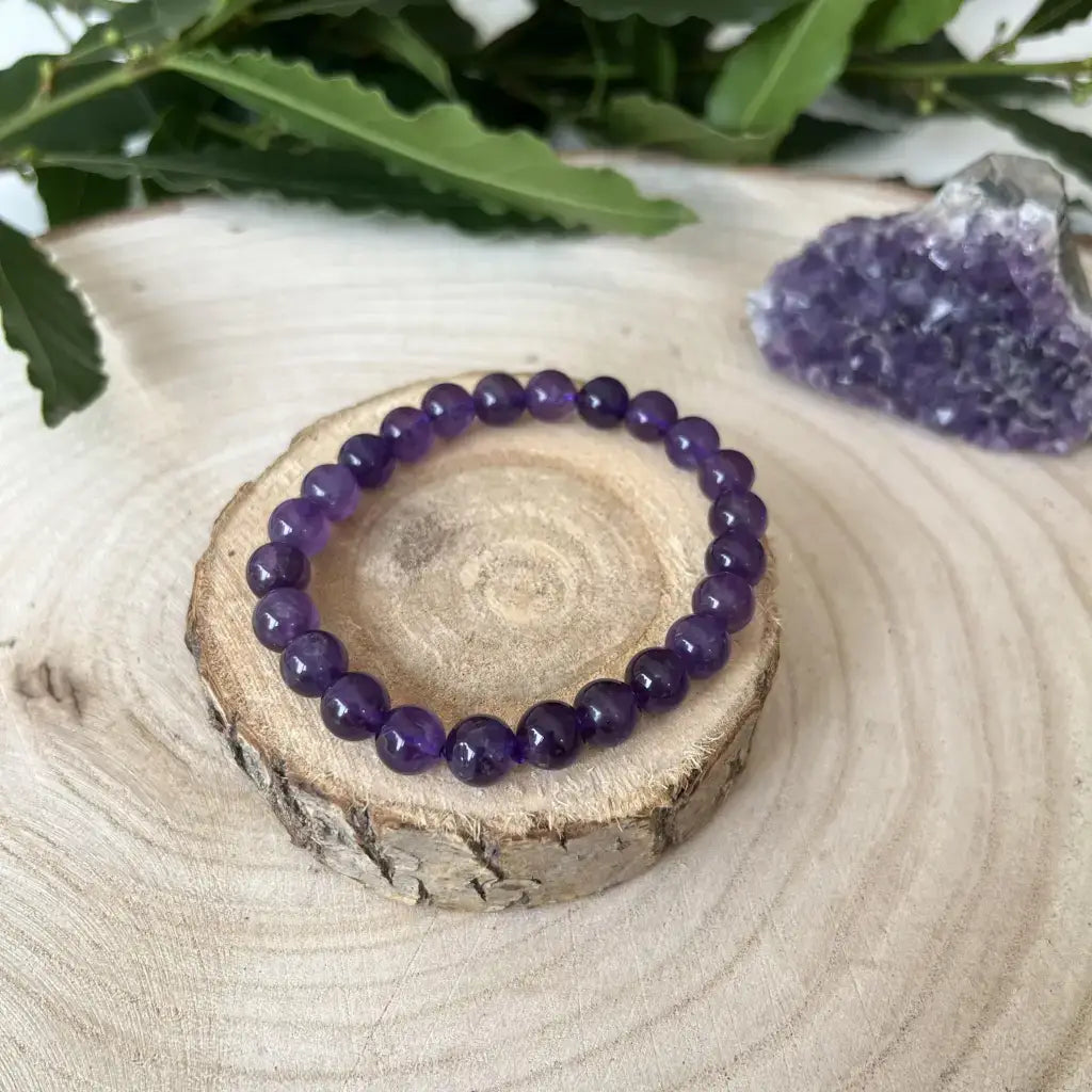 Bracelet Améthyste sur une rondelle en bois, accompagné de cristaux d'améthyste en arrière-plan