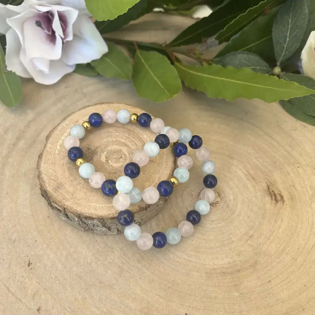 Bracelet d’Amitié en Pierres Naturelles multi-couleurs sur une planche en bois avec des fleurs en arrière-plan