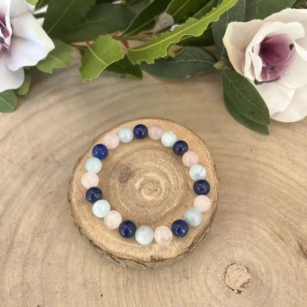 Bracelet d’Amitié en Pierres Naturelles multicolores sur support en bois avec des fleurs en arrière-plan
