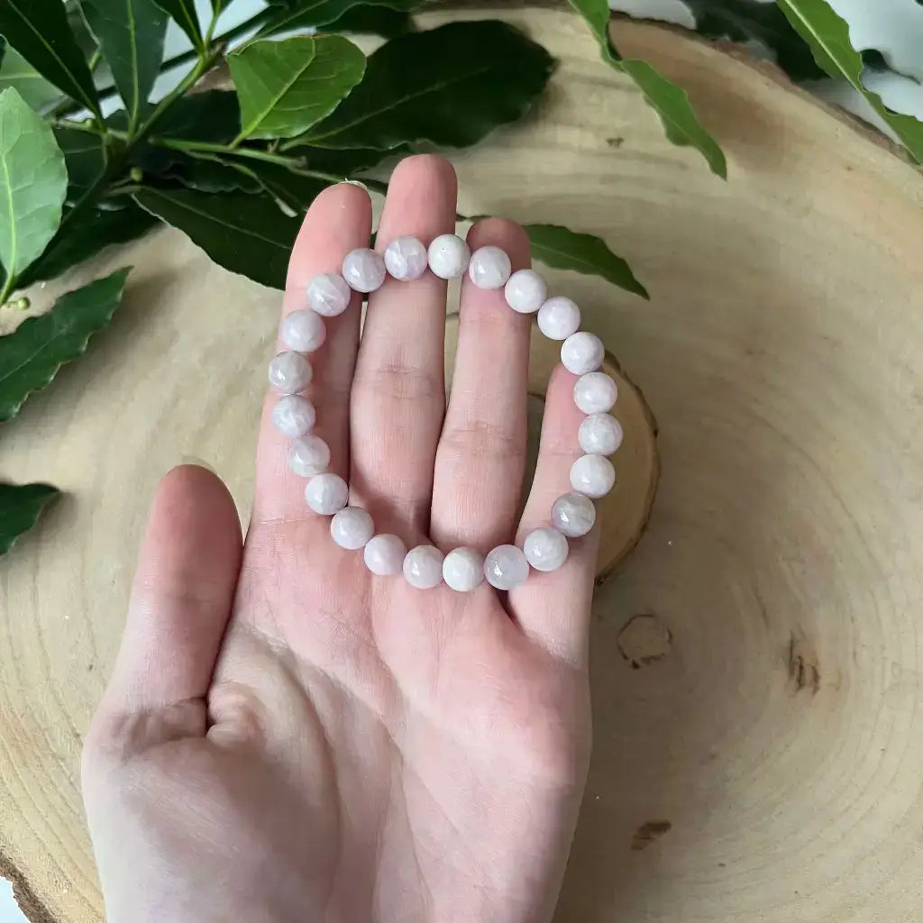 Bracelet en Kunzite élégant, en perles roses, confortablement porté dans la main sur un fond en bois.