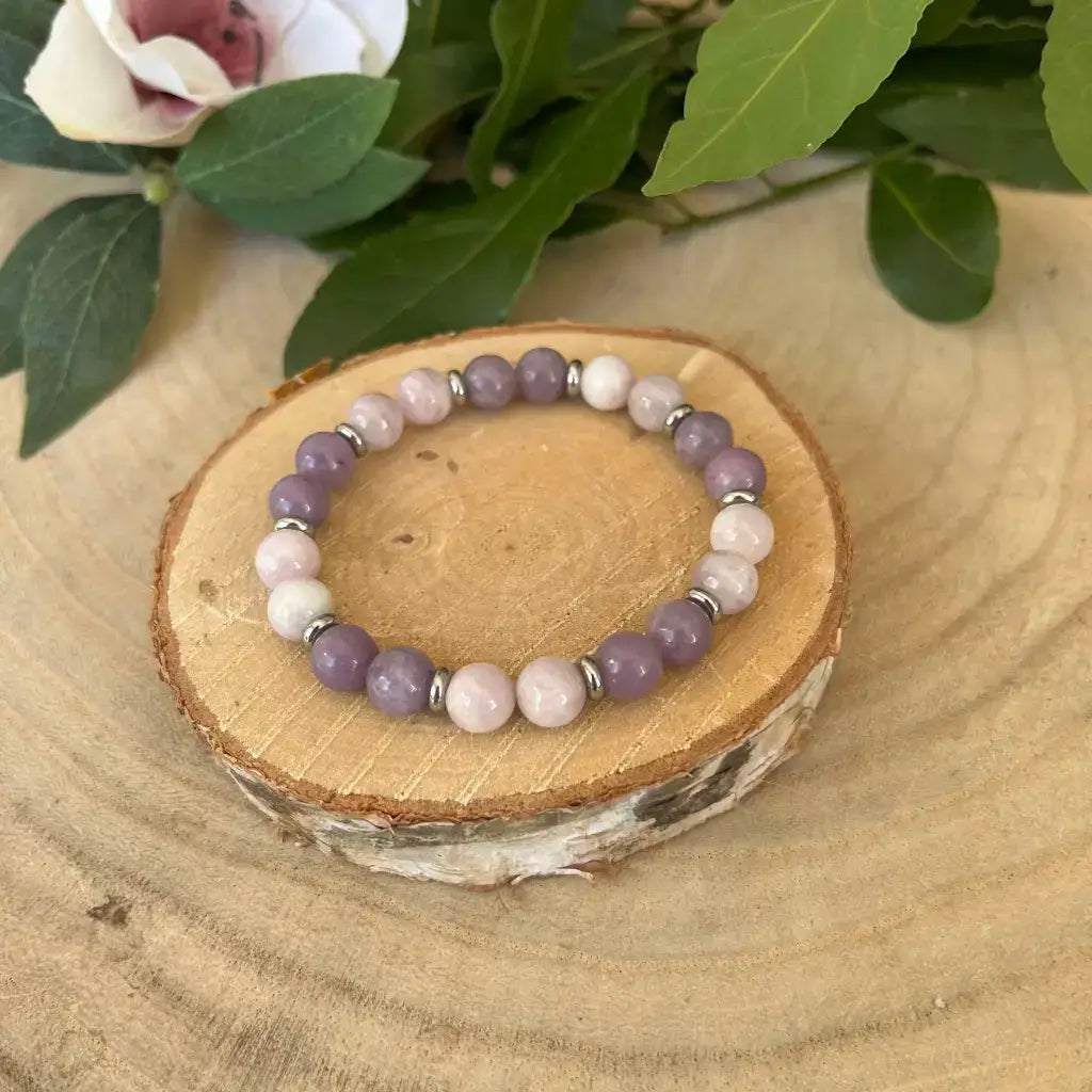 Bracelet kunzite lépidolite d'Aura de Roche avec perles mauves et roses sur un support en bois