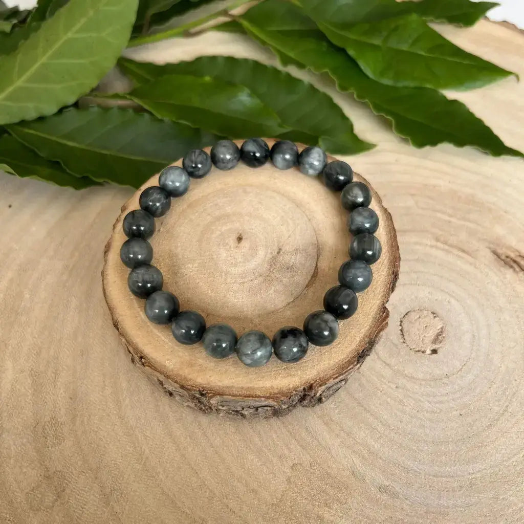 Bracelet Oeil de Chat en pierres naturelles sur support en bois avec feuillage en arrière-plan