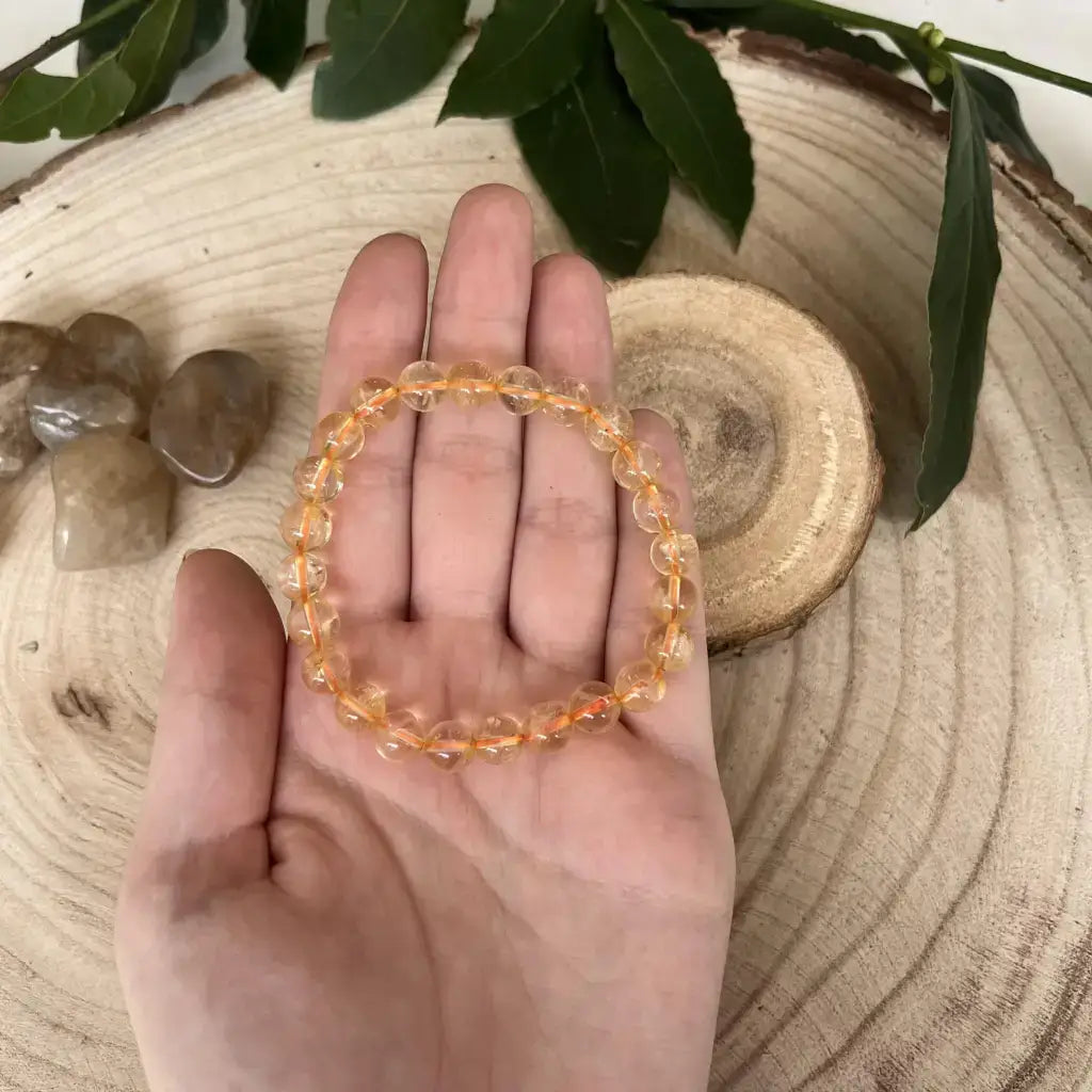 Bracelet Perle Citrine en cristaux brillants, porté à la main sur un fond naturel en bois