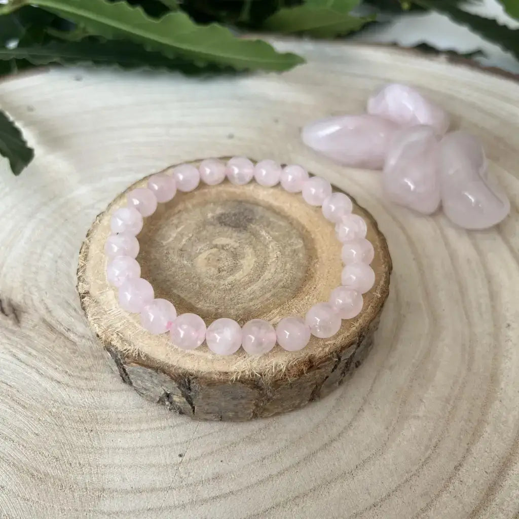 Bracelet Quartz Rose - Amour et Douceur sur un support en bois, avec des pierres de quartz rose en arrière-plan