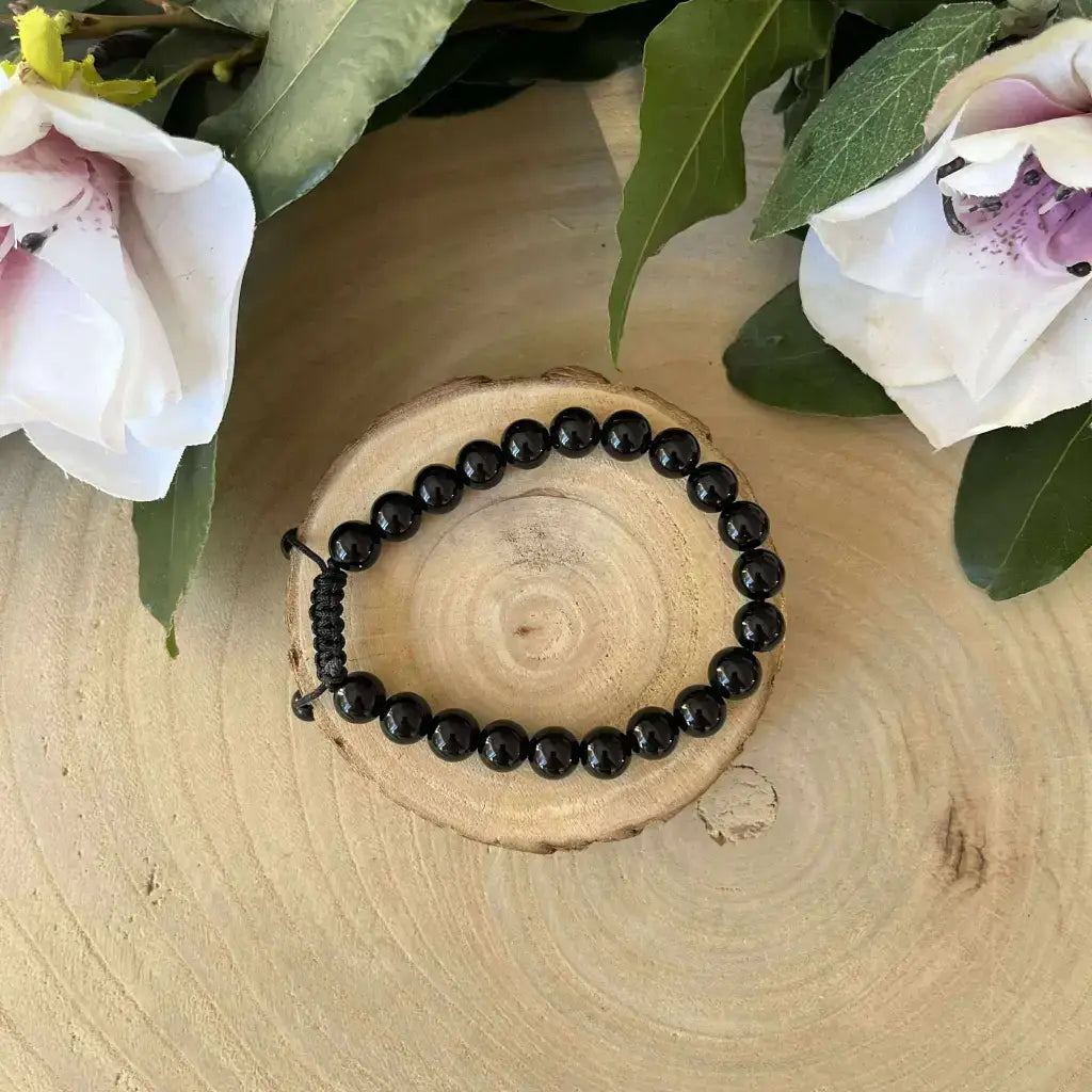 Bracelet Shambala Obsidienne Noire avec perles brillantes sur fond en bois et fleurs délicates