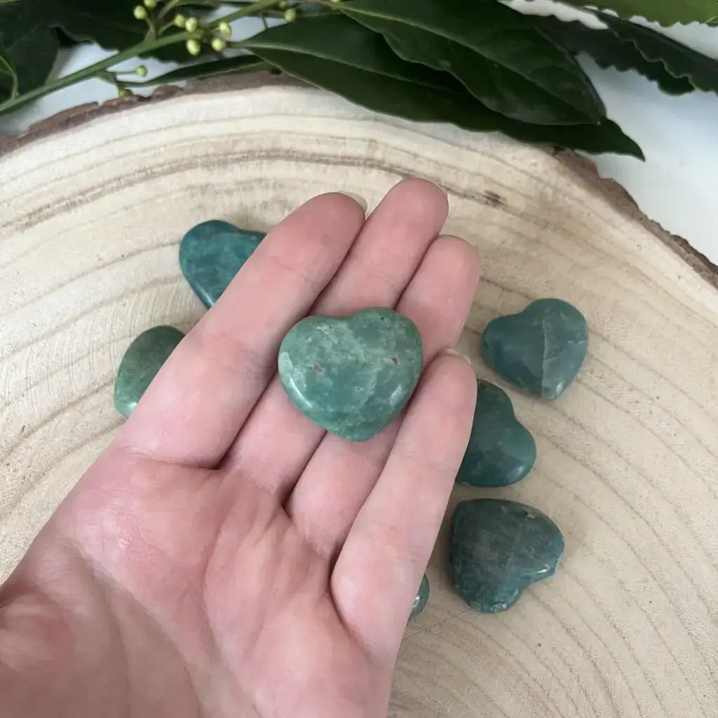 Coeur Amazonite Pierre Naturelle en main avec plusieurs pierres roulées en arrière-plan