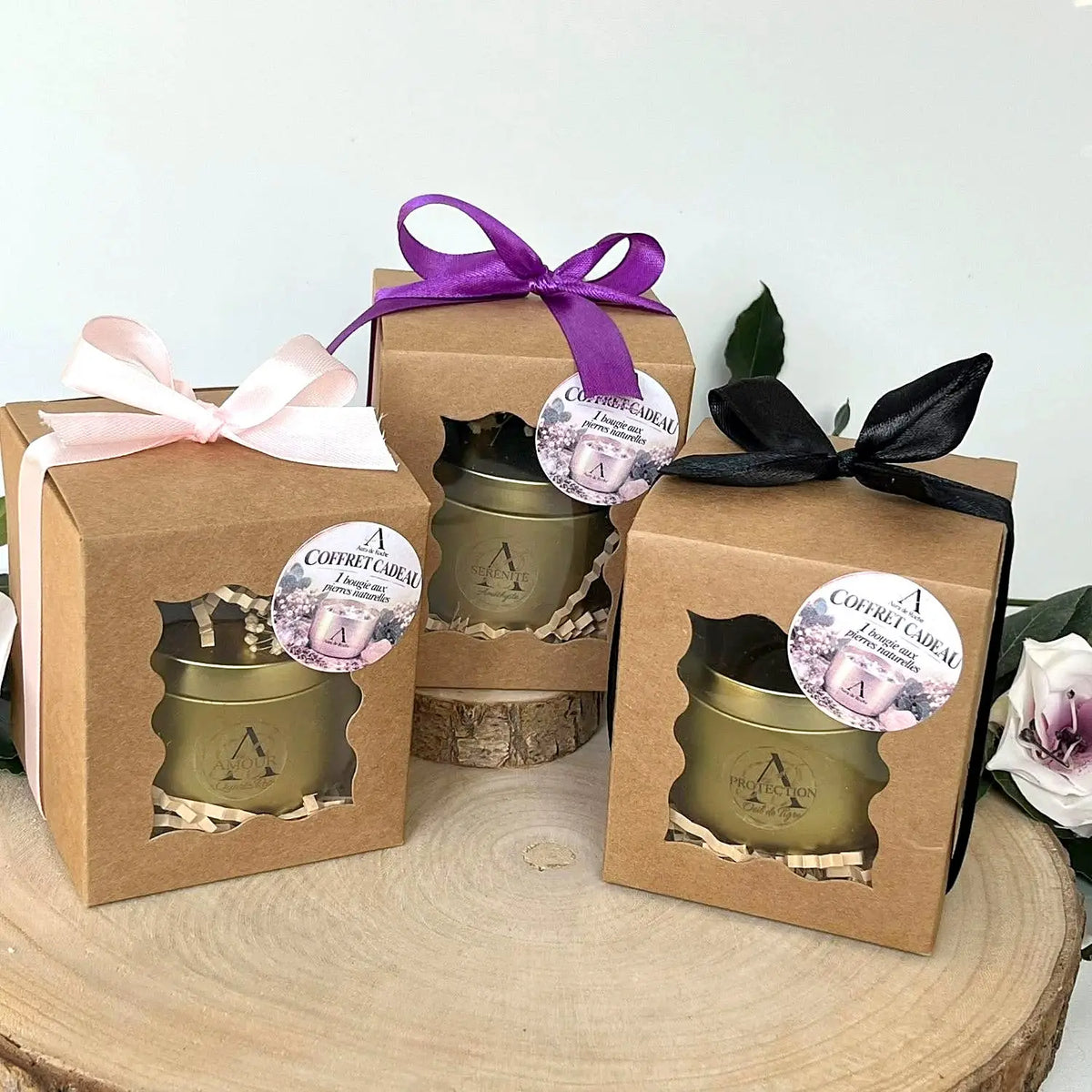 Trois coffrets cadeaux en kraft avec une bougie aux pierres naturelles, rubans rose, violet et noir