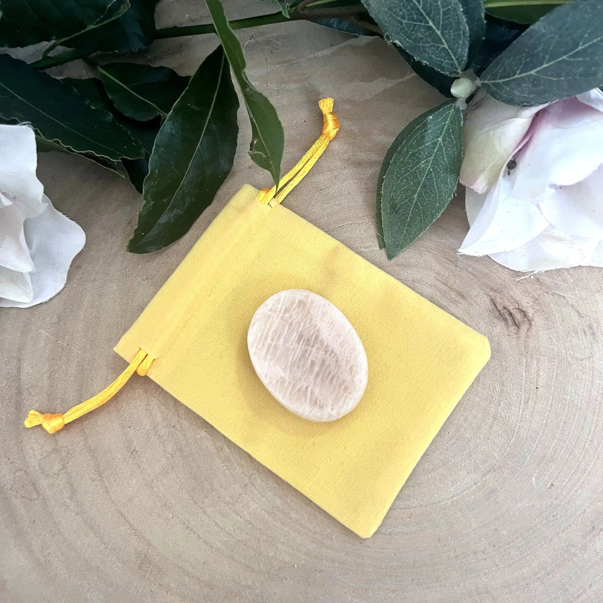 Galet anti-stress en pierre de lune beige posé sur son pochon jaune