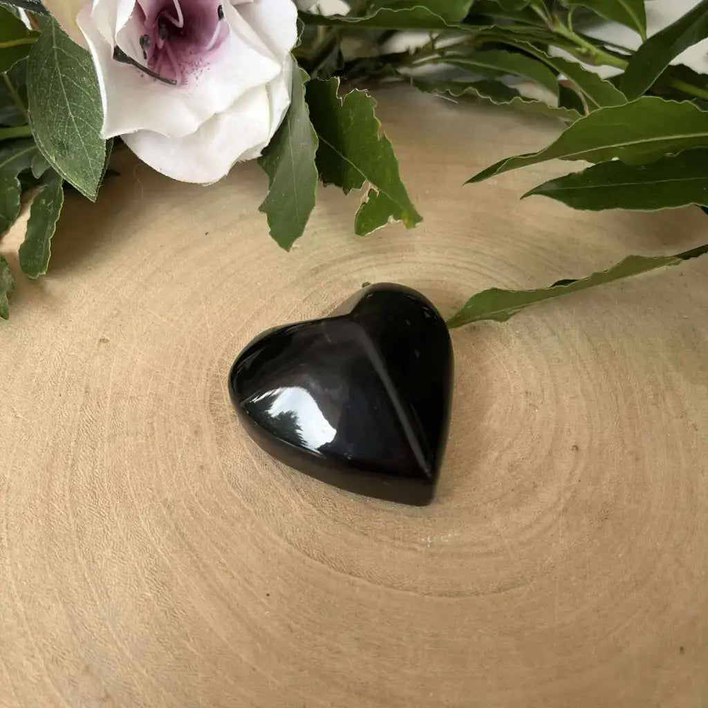 Galet en forme de cœur – Obsidienne Œil Céleste. Galet poli noir sur tranche de bois avec fleur et feuillage décoratif