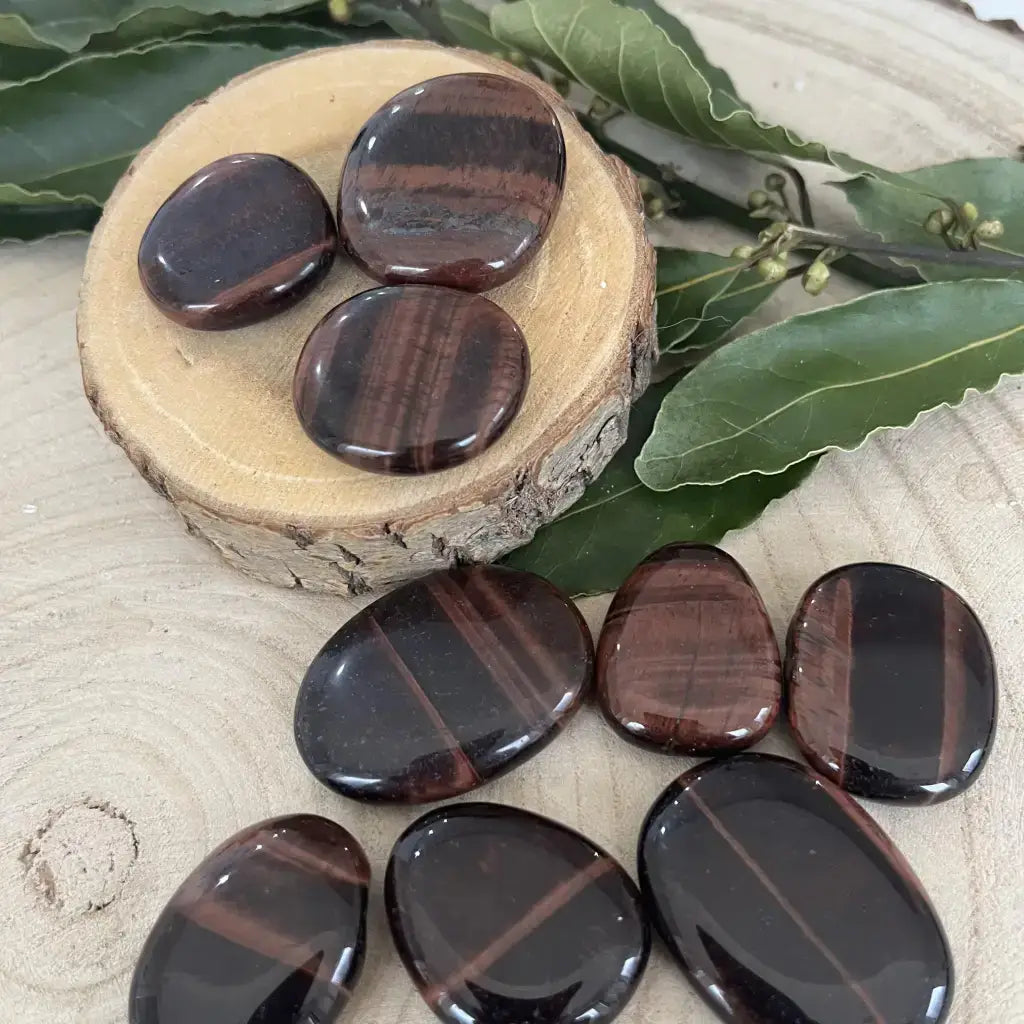 Galet Œil de Taureau polis brun rouge posé en groupe sur tranche de bois avec feuilles Aura de Roche