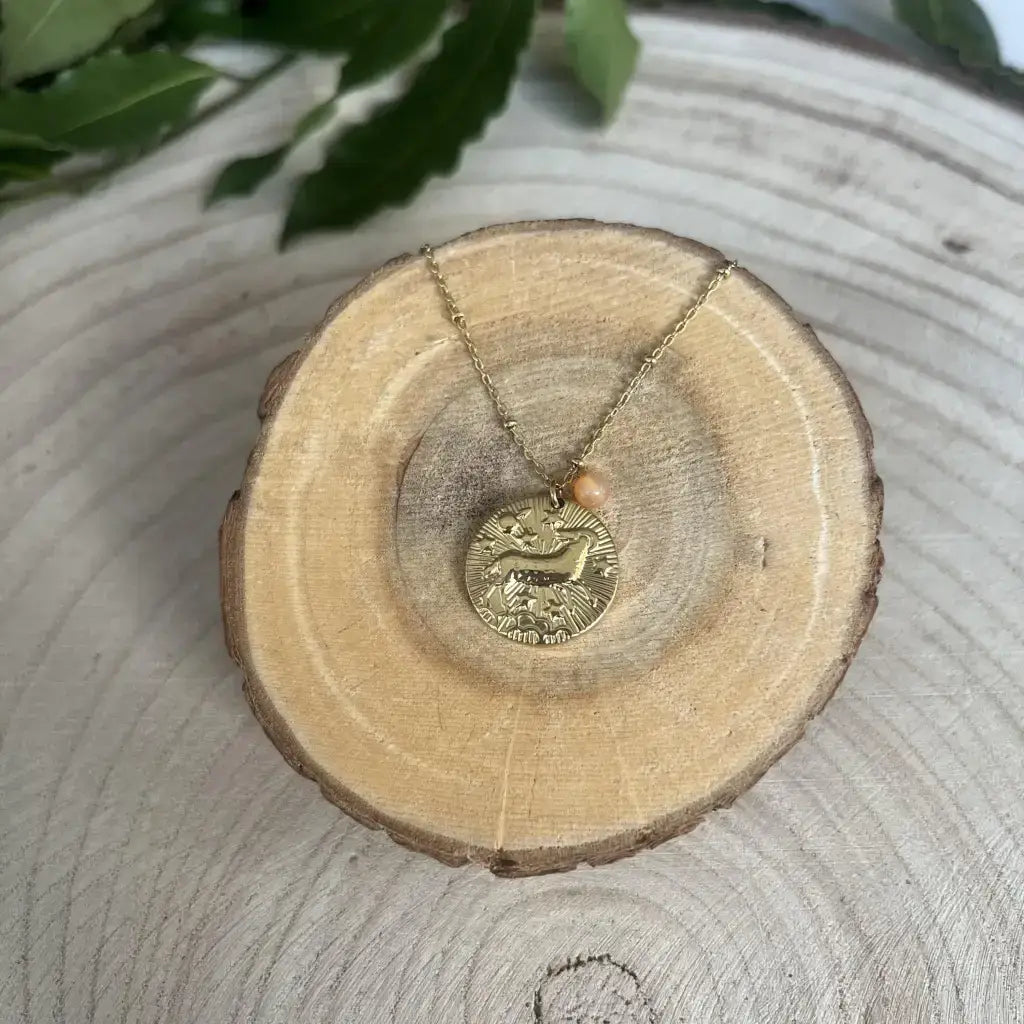 Pendentif Bélier avec Pierre de Pouvoir sur une chaîne dorée, sur un support en bois naturel