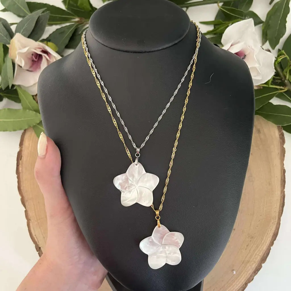 Colliers pendentifs Fleur en Nacre avec chaînes dorée et argentée présentés sur un support noir