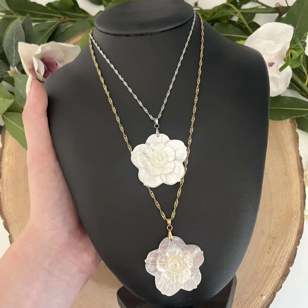 Pendentif Fleur en Nacre Aura de Roche sur chaîne argentée et dorée présenté sur un support noir